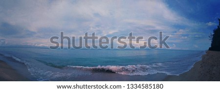 Nature background of Early morning before sunrise at calm ocean with soft waves touching dark beach under white cloudy blue sky, Andaman Sea in Thailand. Dramatic scary sea beach of stormy season.