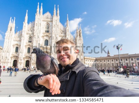 Winter travel, vacations and birds concept - Handsome male tourist with funny pigeons making selfie photo in front of the famous Duomo cathedral in Milan.