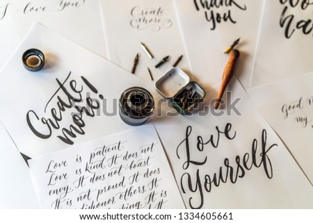 Paper, ink, calligraphy pens and inscriptions. Lettering workshop details. Inscribing ornamental decorated letters. Calligraphy, graphic design, lettering, handwriting, creation concept
