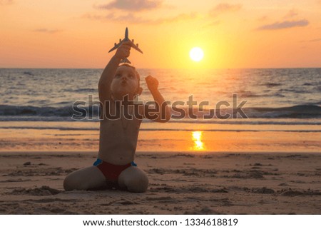 Little baby boy is playing with toy plane on the sand of amazing tropical beach of Andaman sea in Thailand at sunset. Concept of travel by plane with children. Family holidays.