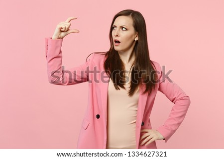 Portrait of concerned puzzled young woman in jacket gesturing demonstrating size with workspace isolated on pastel pink wall background. People sincere emotions, lifestyle concept. Mock up copy space