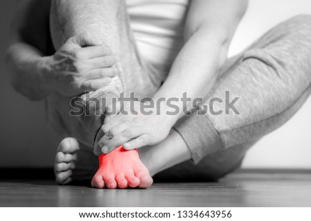 Causian man holds hands to his painful feet, pain in foot.  Black and white photography. red color is area of pain