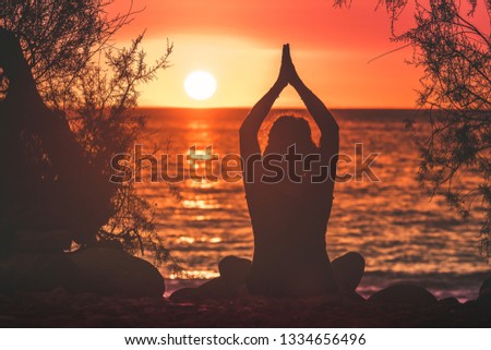 Silhouette image of a young woman making yoga lotus pose on a beautiful summer evening Back view of Girl with hands clasped sunset in background and and branches that frame Enjoyable romance feelings 
