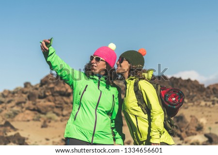 Two young brunette girls smiling and taking a selfie. A couple of women talk with remote friends with smartphone wifi technology Female enjoying a beautiful day of trekking outdoors in mountain desert