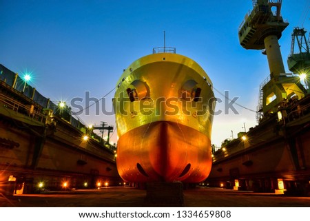 Shipyard front view of cargo ship, front boat, both rope and anchor at forward during repair, maintenance in floating dry cock on twilight background.