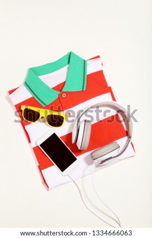 Smartphone with headphones, sunglasses and striped t-shirt on beige background