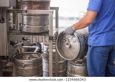 Man holding steel beer kegs on the production line in the factory