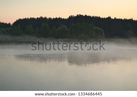 The river is covered with fog. Boat with fishermen in the fog on the river. Fishermen on a boat are fishing early in the morning. The picture was taken from another boat