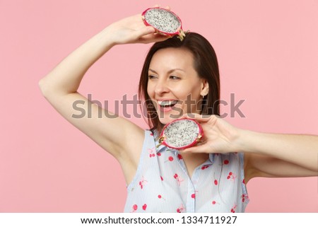 Smiling young girl in summer clothes looking aside, hold half of fresh ripe pitahaya dragon fruit isolated on†pink pastel background. People†vivid lifestyle relax vacation concept. Mock up copy space