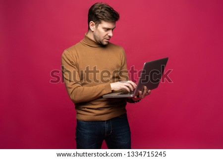 Picture of handsome man in casual holding laptop and chatting or working isolated over pink background