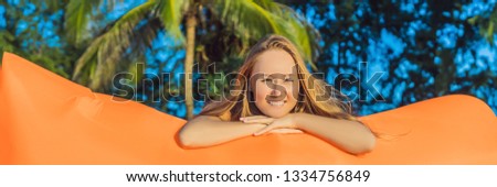 Summer lifestyle portrait of pretty girl sitting on the orange inflatable sofa on the beach of tropical island. Relaxing and enjoying life on air bed BANNER, LONG FORMAT