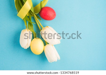 Easter blue background with white tulips and varicoloured dyed Easter eggs. Postal
