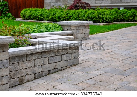 A seat wall with pillars and natural stone coping helps define a tumbled paver driveway and is a beautiful landscaping feature. Royalty-Free Stock Photo #1334775740