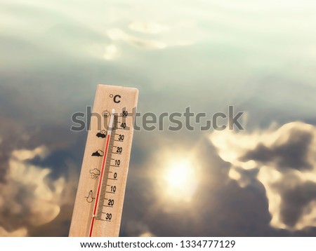 Thermometer showing 30 degrees of heat against the backdrop of lake water with the reflection of clouds and the sun. Royalty-Free Stock Photo #1334777129