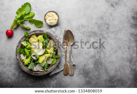 Green vegetables salad with avocado, kale, sprouting herbs in rustic bowl served with sauce, gray concrete background, close-up, top view. Healthy clean eating, diet/detox concept with space for text