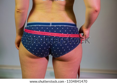 The girl with excess weight measures the ass with the tape. Female body, rear view, on gray background. Polka Dot Panties