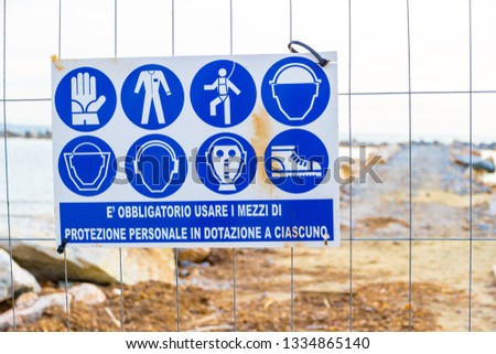 Warning sign reading: 'protective equipment must be worn' near a construction site on the shoreline in Follonica, Italy