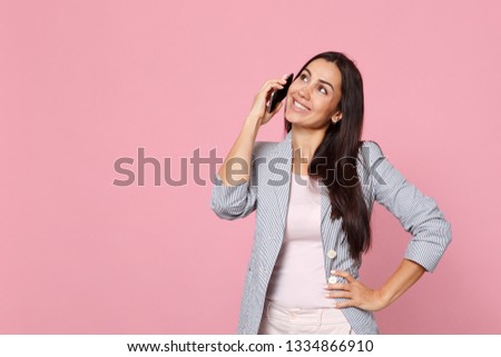 Pretty young woman in striped jacket talking on mobile phone, conducting pleasant conversation isolated on pink pastel wall background. People sincere emotions lifestyle concept. Mock up copy space