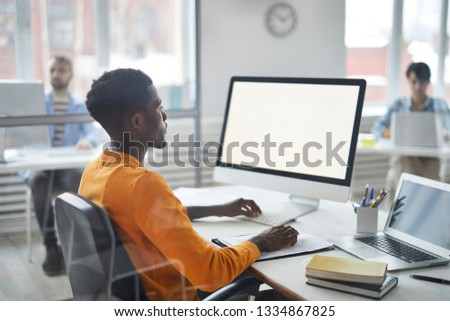 Young casual African-american businessman looking at computer screen while analyzing online data by desk