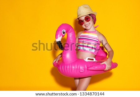 happy child girl in swimsuit with swimming ring flamingo on a colored yellow background
