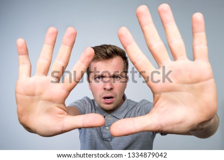 Young european man in gray t-shirt showing with hand stop timeout gesture. Negative facial emotion