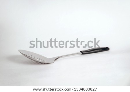 A silver spoon with holes to pull food from the pot. The concept of eating, using kitchen items while cooking. Supporting special devices during cooking, preparing a meal.