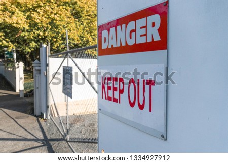 "Danger - Keep Out" Sign in front of locked fence gate.
