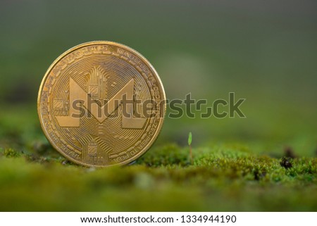 Monero XMR cryptocurrency physical coin placed on the green grass and moss. Framed on the left side of the picture.