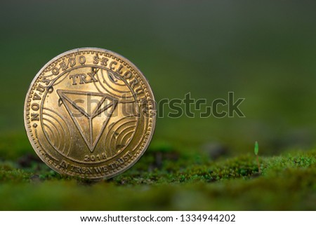 Tron TRX cryptocurrency physical coin placed on the green grass and moss. Framed on the left side of the picture.