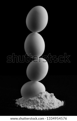 Balanced and Staked Eggs in White Flower on Black Backdrop