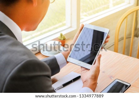 Business man sitting and looking at screen of tablet . Coffee, notebook and smart phone also on the desk