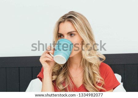 Caucasian blonde having a cup of coffee, tea, soup or hot chocolate in bed.