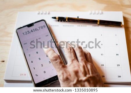 Schedule plan, hand  using calculator and pen on calendar isolated on wood texture background can be used in article of business and financial  Royalty-Free Stock Photo #1335010895
