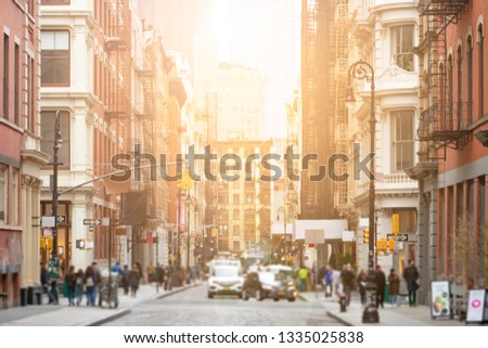 Busy intersection of Broome and Greene Streets is crowded with people and cars in the SoHo neighborhood of New York City with sunlight background