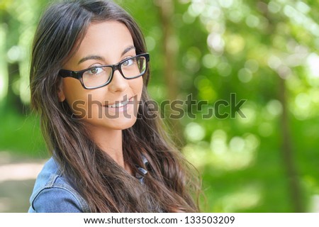 Portrait of beautiful smiling dark-haired young woman, against summer green park. Royalty-Free Stock Photo #133503209