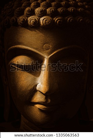 The head of Buddha statue Made of golden sandstone with black background and soft light-image