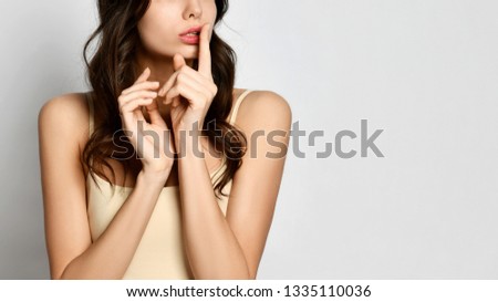 Close-up. Woman holds her finger at her mouth and make shhh like asks to speak softly, keep silence or a secret on gray background with text space.