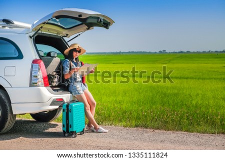 woman traveler sitting on hatchback of car and reading a map during go to travel on  holiday background is the green fields.