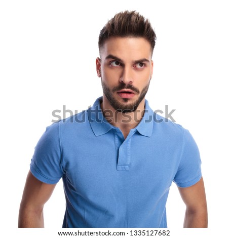Young man wearing a light blue polo trying to remember something while looking upwards and to a side on a light background