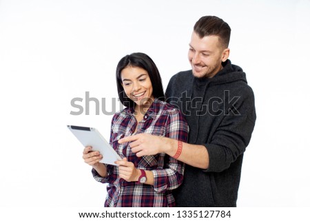 Closeup photo of young couple looking at tablet and pointing on the screen, wearing casual street wear, isolated on white background
