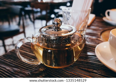 Teapot for the glass close up with cafe background, hot tea in the teapot over wooden table with mugs. Great for design, lettering, blogs.