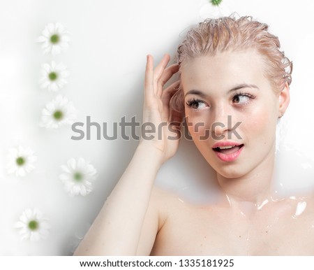 relaxed girl lying in a spa bath with milk and daisies