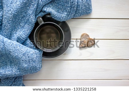 A blue knitted sweater and a cup of coffee with a shortbread in the shape of a broken heart. Flat lay, top view, there is space for your text.