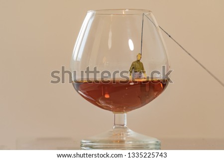 Miniature man figure hanging in the glass of brandy. Shallow depth of field background. Healthcare and alcoholism concept.