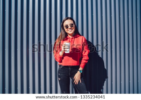 Half length portrait of cheerful Asian hipster girl dressed in red hoody holding takeaway cup with coffee, concept of millennial people lifestyle. Coffee culture. Copy space area for text message