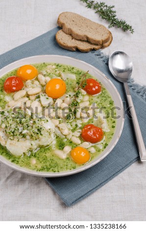 Stewed beans with fish and green sauce in a bowl on a textile background. Selective focus.