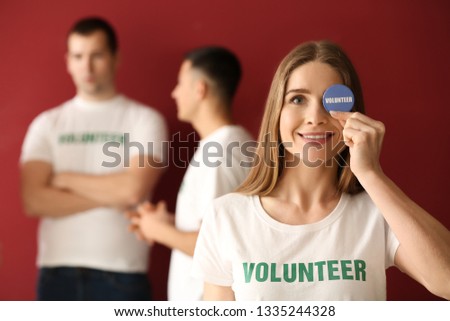Young female volunteer with badge and her team on color background