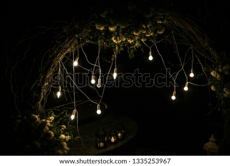White flowers arch at the wedding ceremony. Outdoors decoration. Romantic rustic style. Lamps lights in the evening.