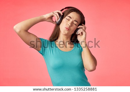 A woman in a blue t-shirt on a coral background listening to music with headphones                         