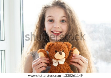 Portrait of a pretty girl with long curly hair. In the hands of the girl a teddy bear.

